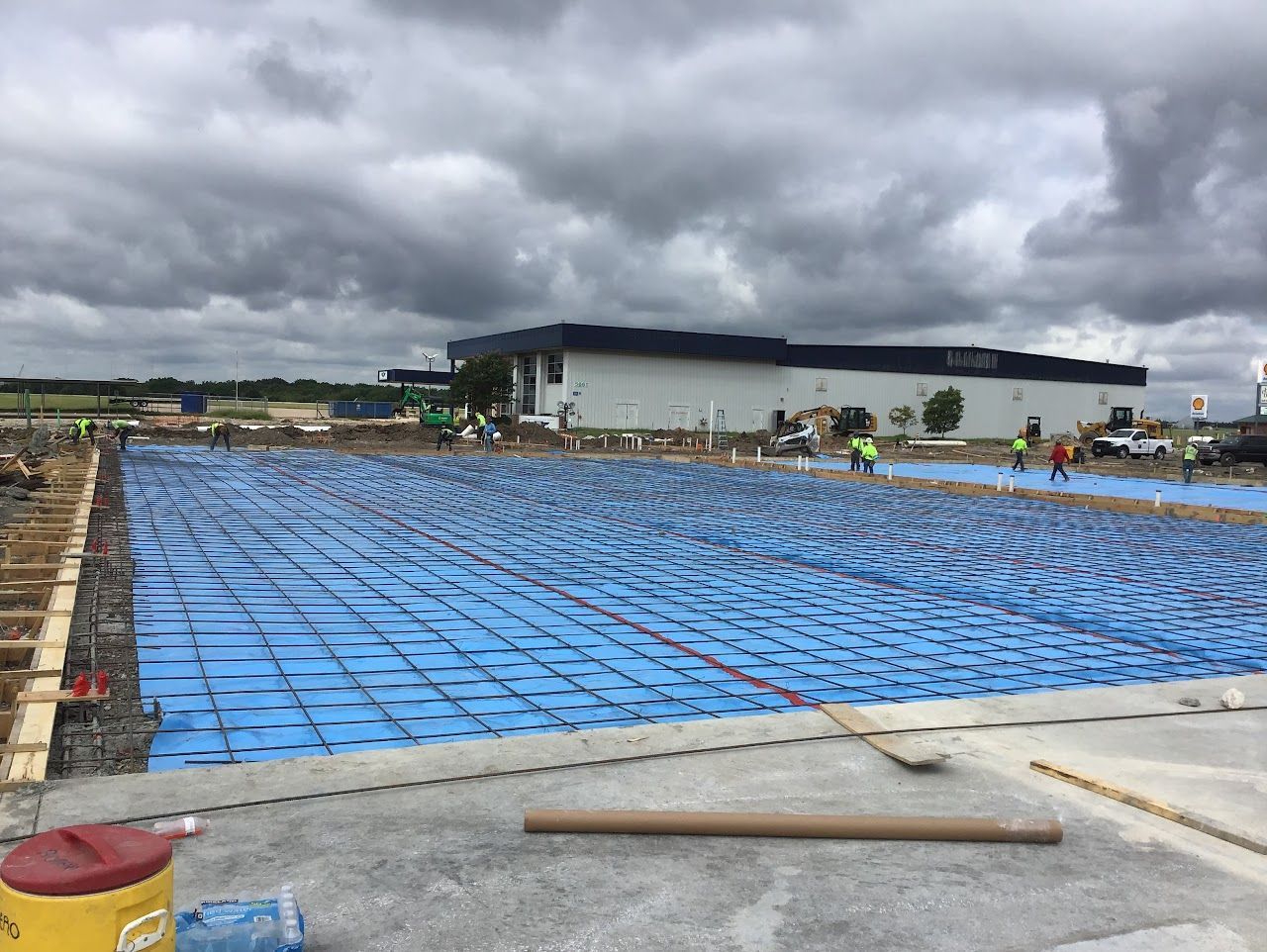 Construction site with blue insulation laid, concrete forms, and a building under a cloudy sky.
