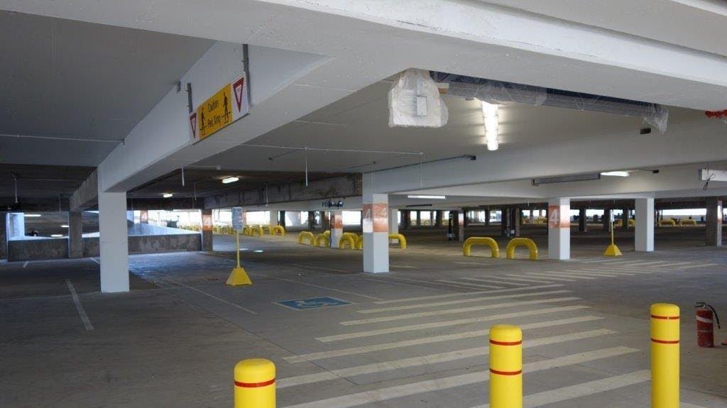 Empty parking garage with yellow and red bollards, white columns, and ceiling lights.