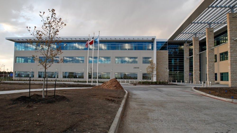 Modern, light-colored brick building with large windows and flags. Cloudy sky above.