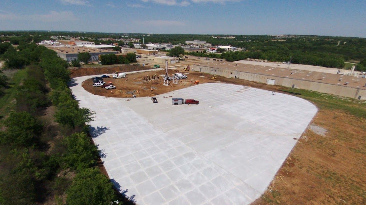 Aerial view of a construction site with concrete surfaces, vehicles, and a partly constructed structure surrounded by trees.