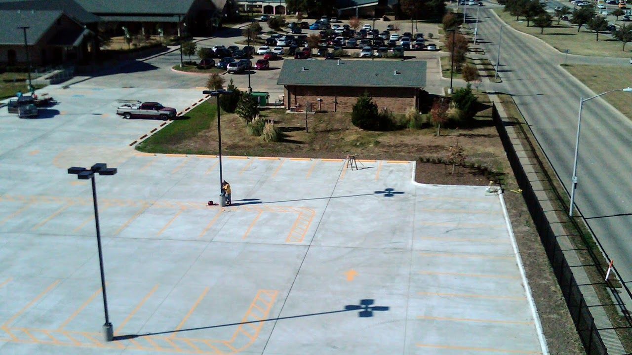 Parking lot with cars, buildings, and a person standing by a light pole on a sunny day.