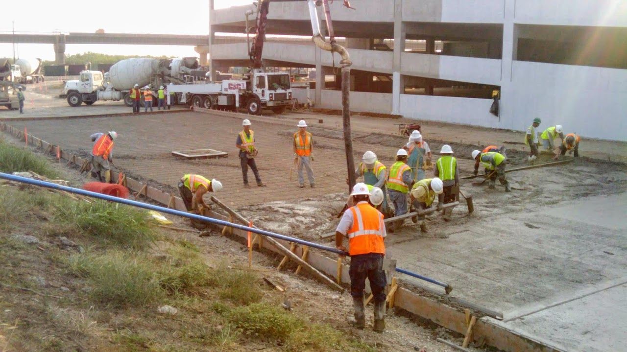 Construction workers pouring concrete at a building site; several people in hard hats and safety vests.