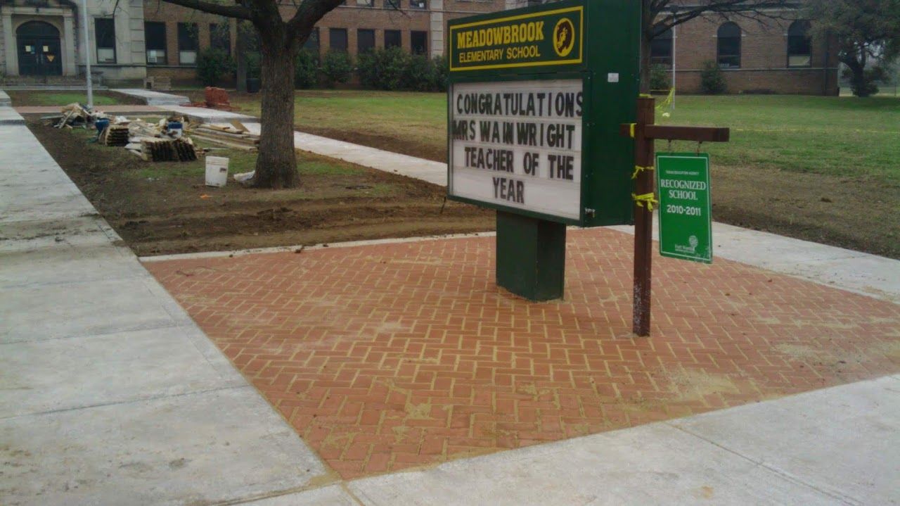 Signboard in front of a school with a brick patio; text: 