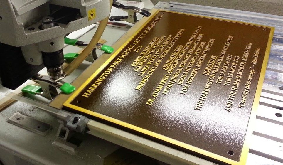 CNC machine engraving a bronze-colored plaque with gold lettering