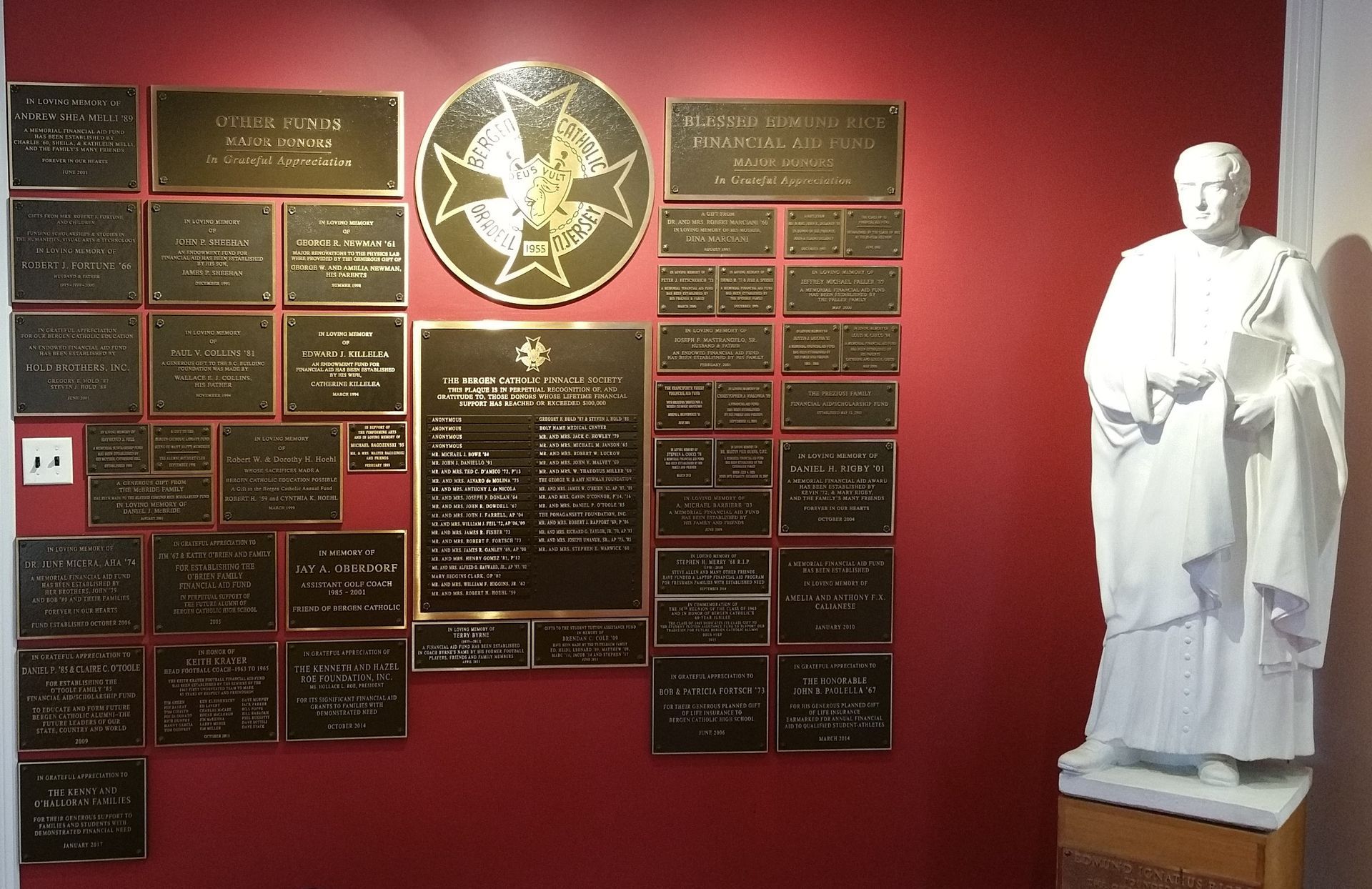 Wall with bronze plaques and a statue of a robed figure on a red wall