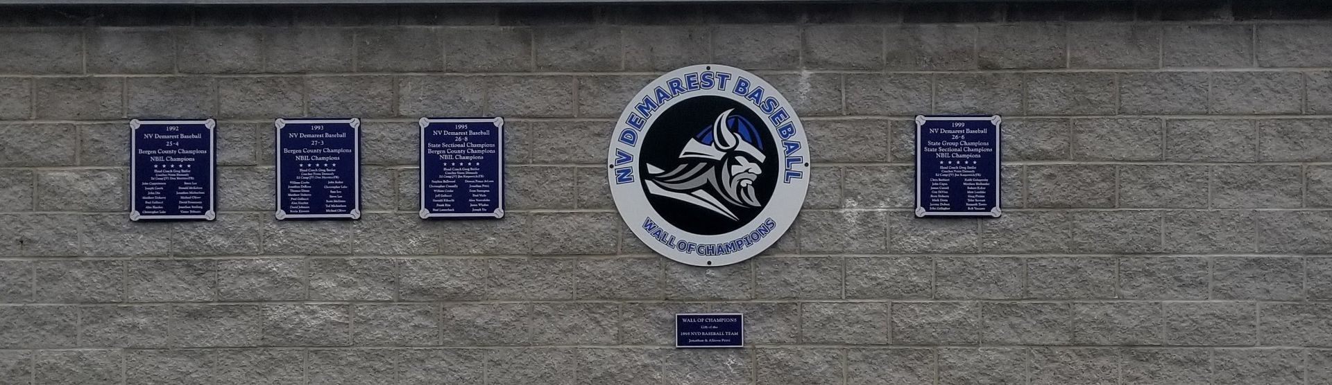 A grey brick wall displays several blue plaques and a circular emblem with a wolf design