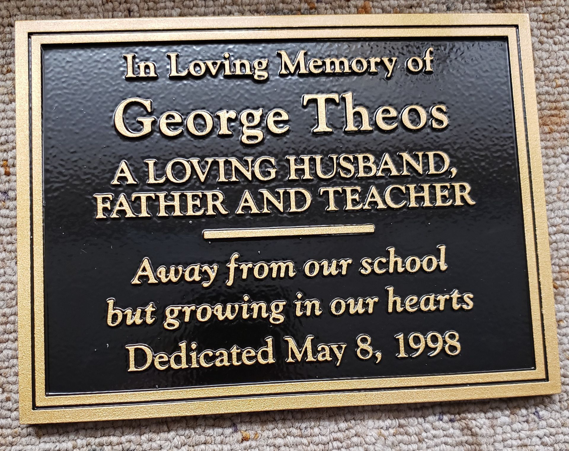 Bronze plaque with gold lettering honoring George Theos, a husband, father, and teacher