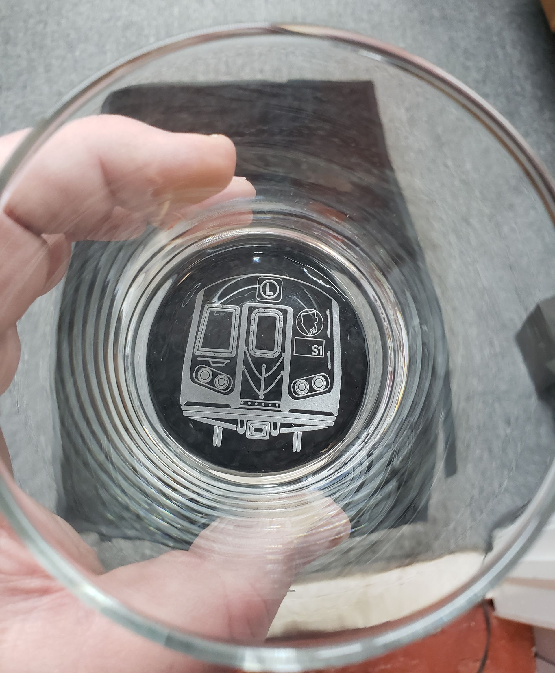 Person holding a clear glass etched with a detailed outline of a subway train car