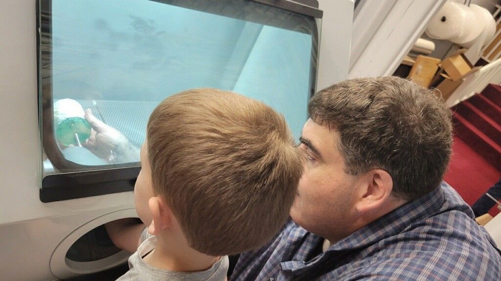 A man and child looking into a window at a light blue and white object