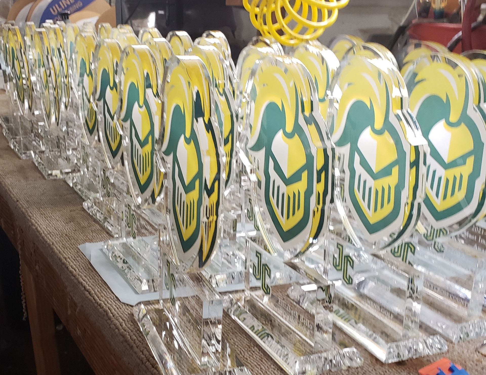 Row of clear acrylic trophies with yellow and green crests on a wooden surface