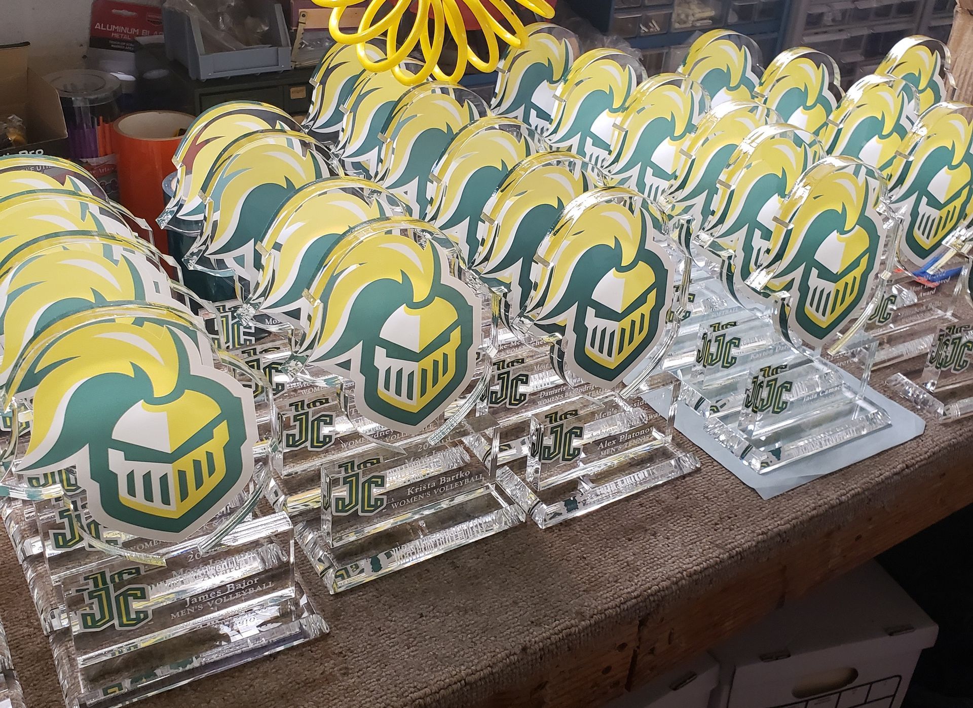 Trophies with a green and yellow Knight helmet logo on clear bases sit on a wooden surface