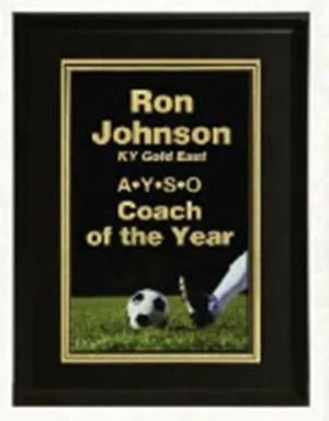 Black plaque with gold text: "Ron Johnson, KY Gold East, AYS O, Coach of the Year." Soccer ball and foot on grass.