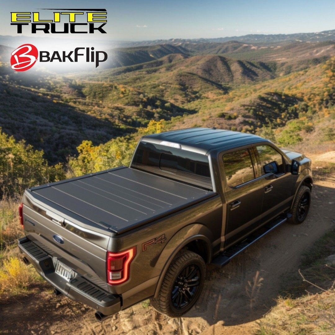 Dark truck with a black folding bed cover driving on a dirt road in a mountainous area.