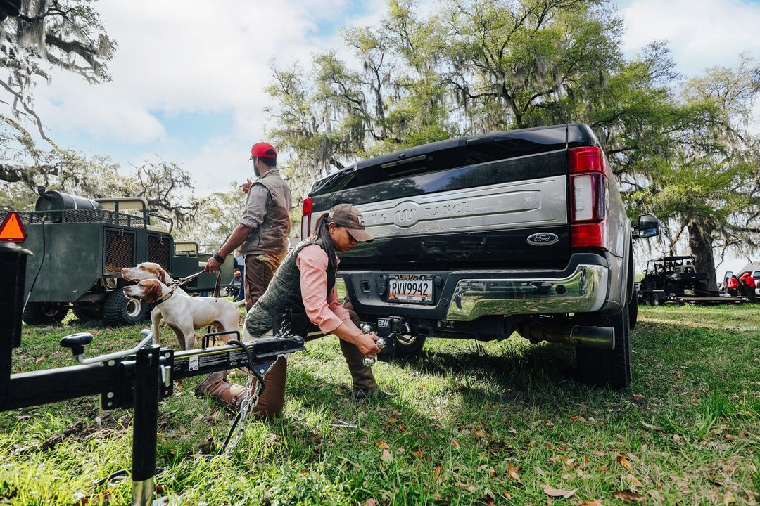 Woman connecting trailer to black truck outdoors, another person nearby.