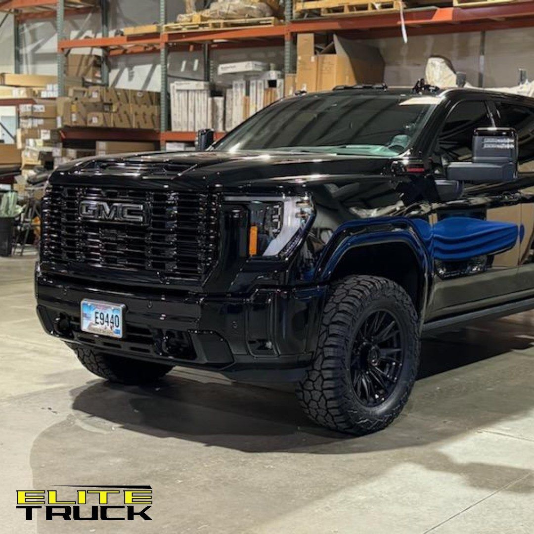 Black GMC Sierra truck with black wheels and a black grille, inside a warehouse.