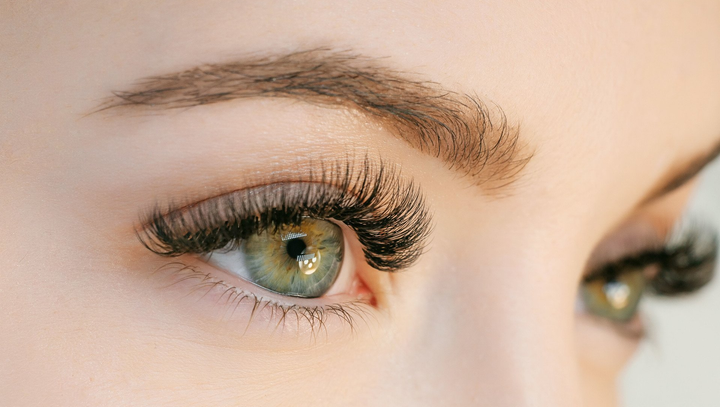 Learn More About Microblading and Lash Tints Close-up of a hazel eye with long false eyelashes and arched eyebrow