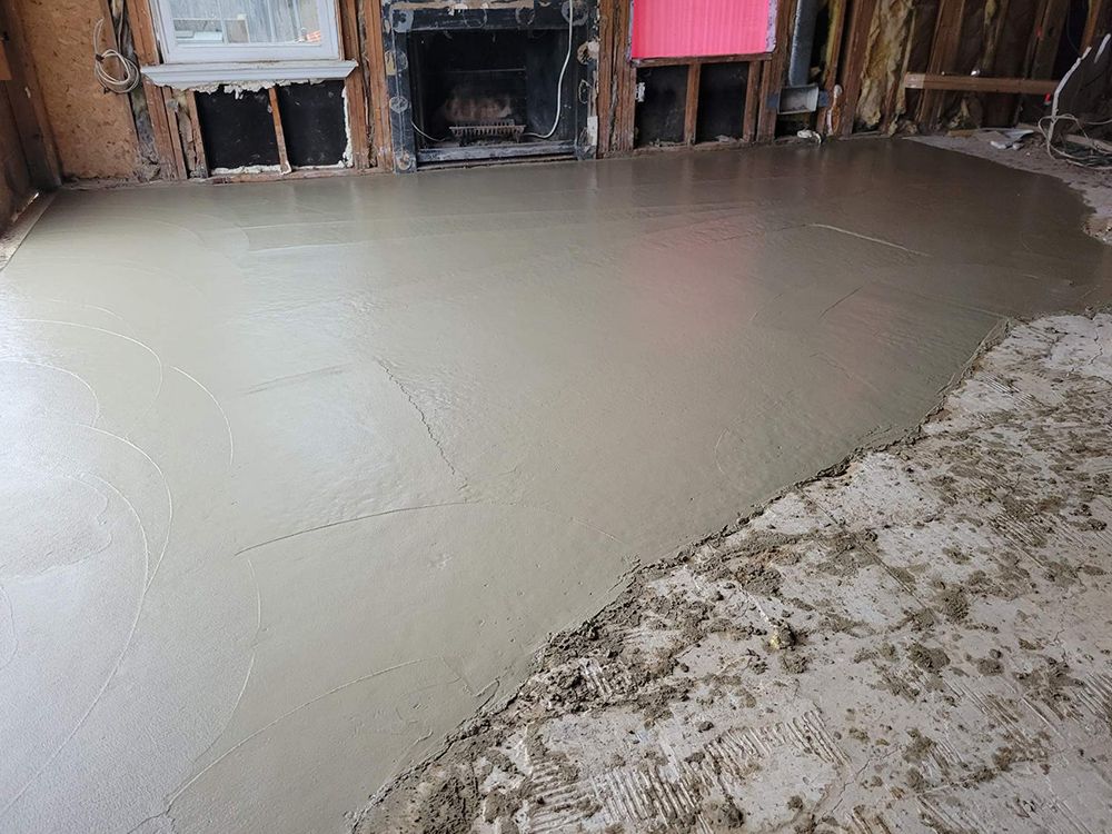 A concrete floor is being poured in a room with a fireplace.