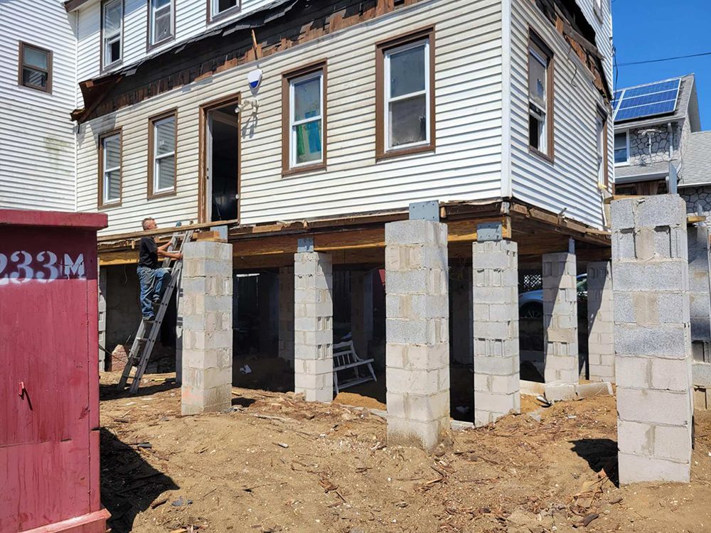 A man is standing on a ladder in front of a house that is being built on stilts.