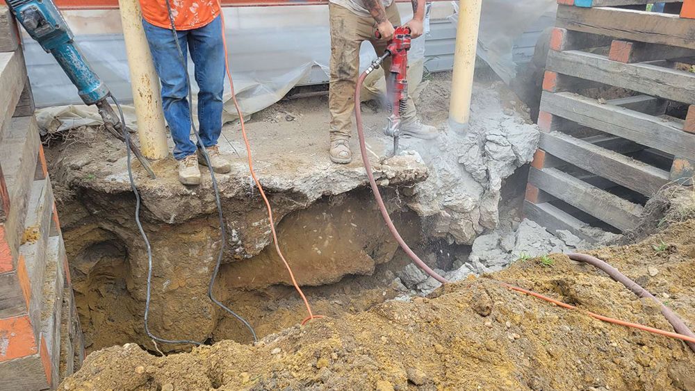 A couple of construction workers are standing in a hole in the ground.