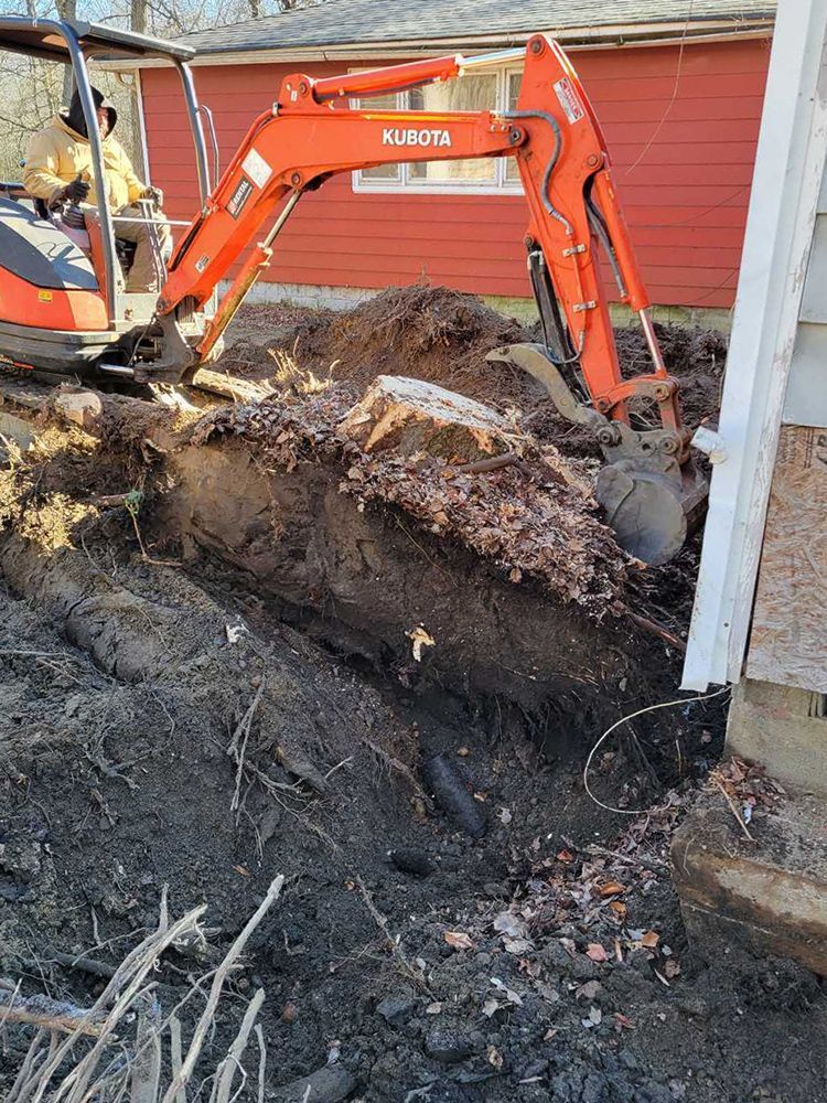 An orange and black excavator is digging a hole in front of a red house.