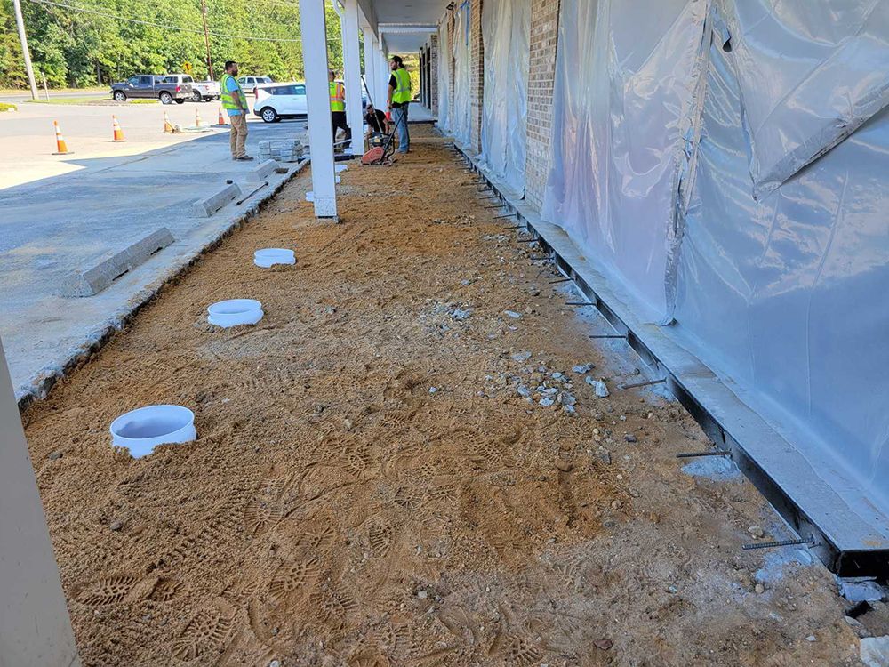 A group of construction workers are working on a sidewalk in front of a building.