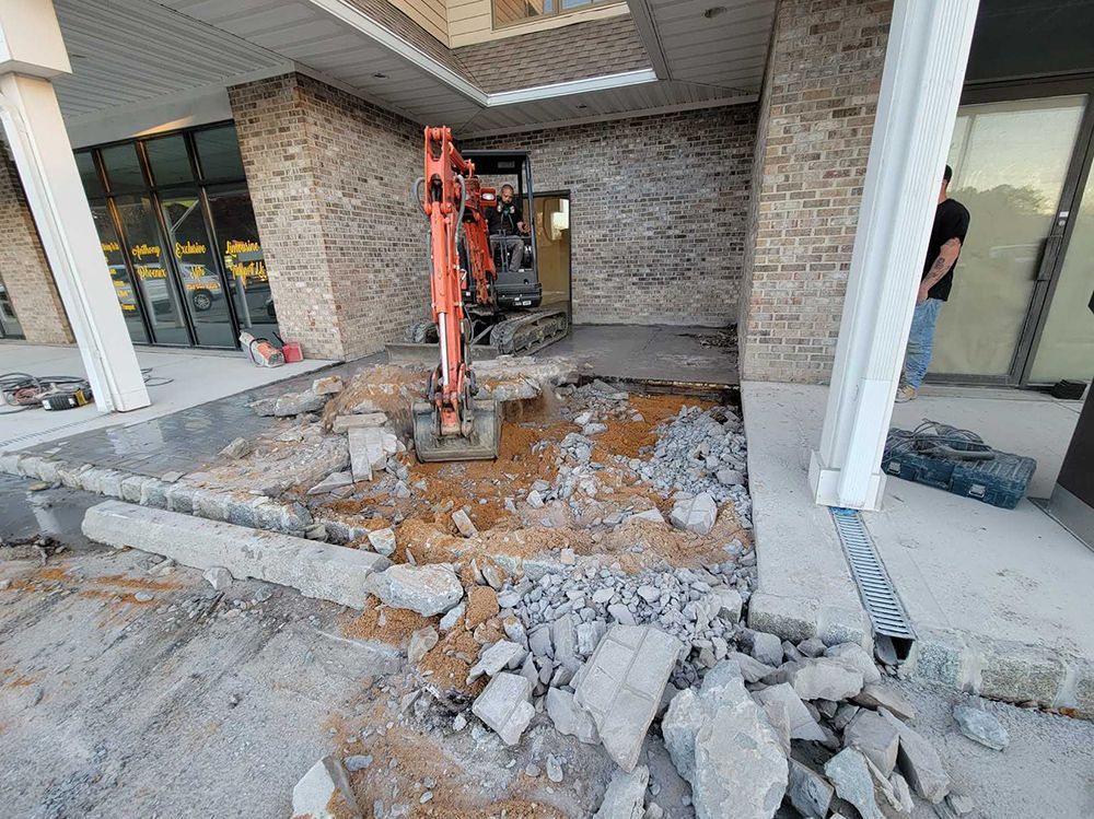 A small excavator is digging a hole in the ground in front of a building.