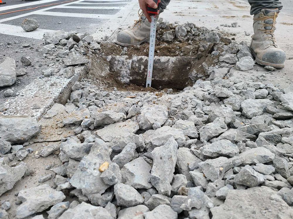 A man is measuring a hole in the ground with a tape measure.