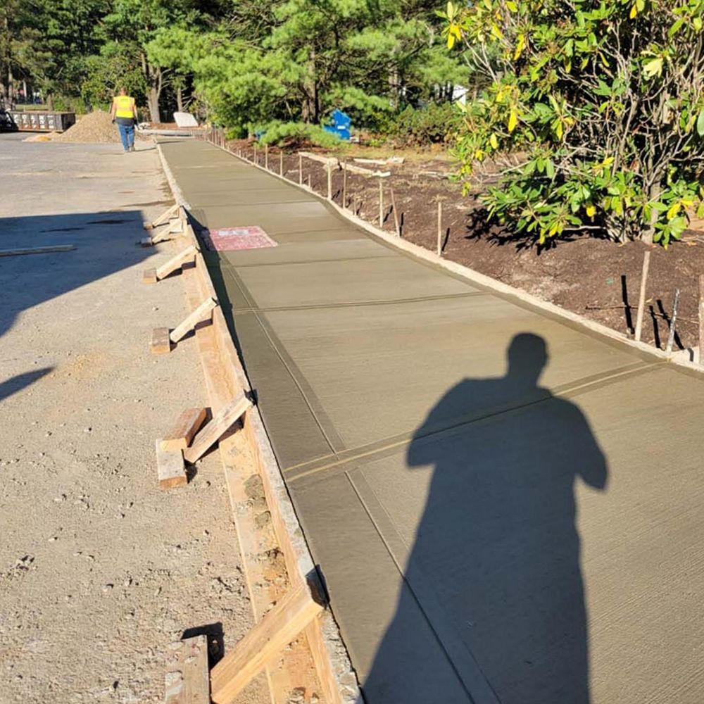 A shadow of a person is cast on a concrete sidewalk.