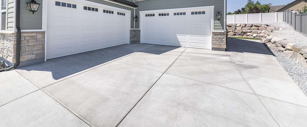 A concrete driveway leading to a garage with two white garage doors.