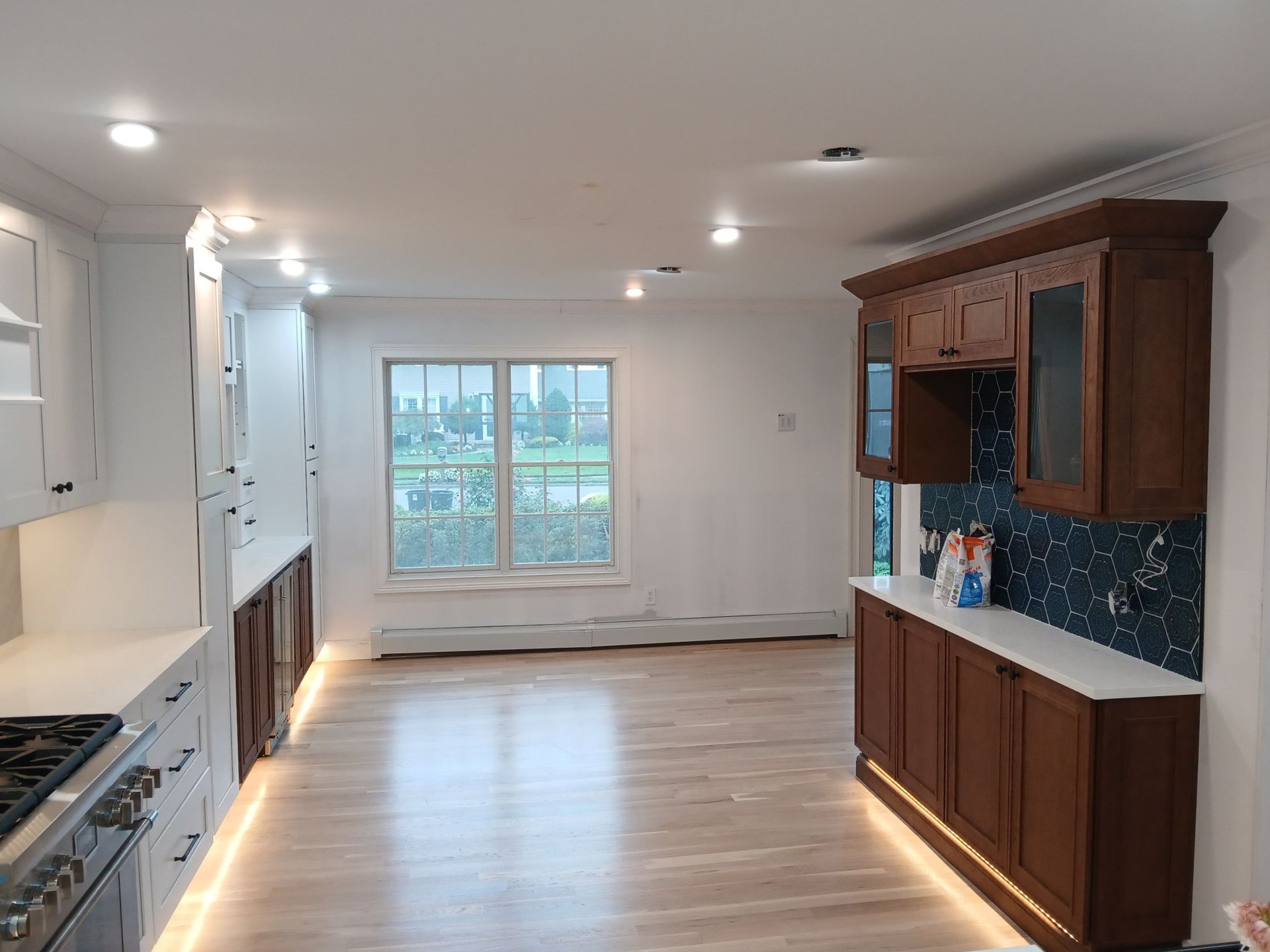A newly renovated kitchen with white and brown cabinets, light wood floors, and a window.