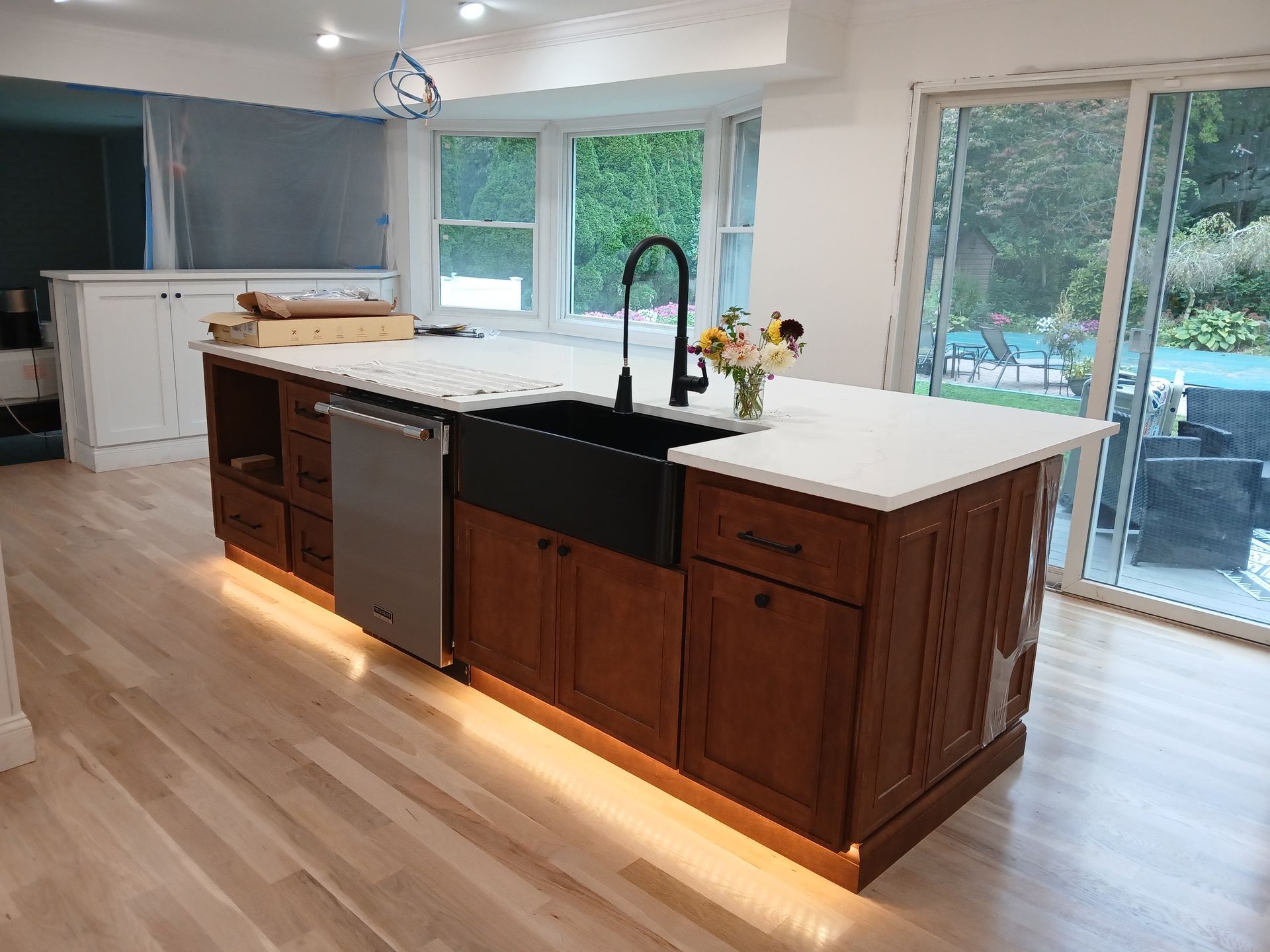 Newly renovated kitchen island with a black sink and faucet, wood cabinetry, and white countertop.