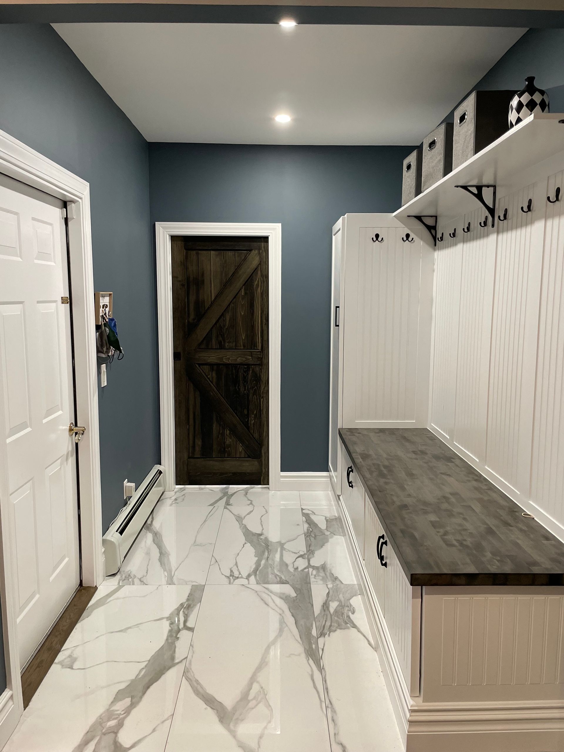 Hallway with blue walls, white trim, marble floor, and a built-in white bench with coat hooks. 