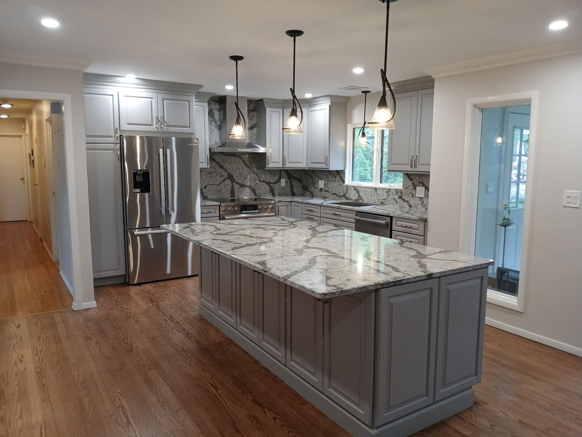 Newly renovated kitchen with gray cabinets, marble countertops, stainless steel appliances, and wood floors.