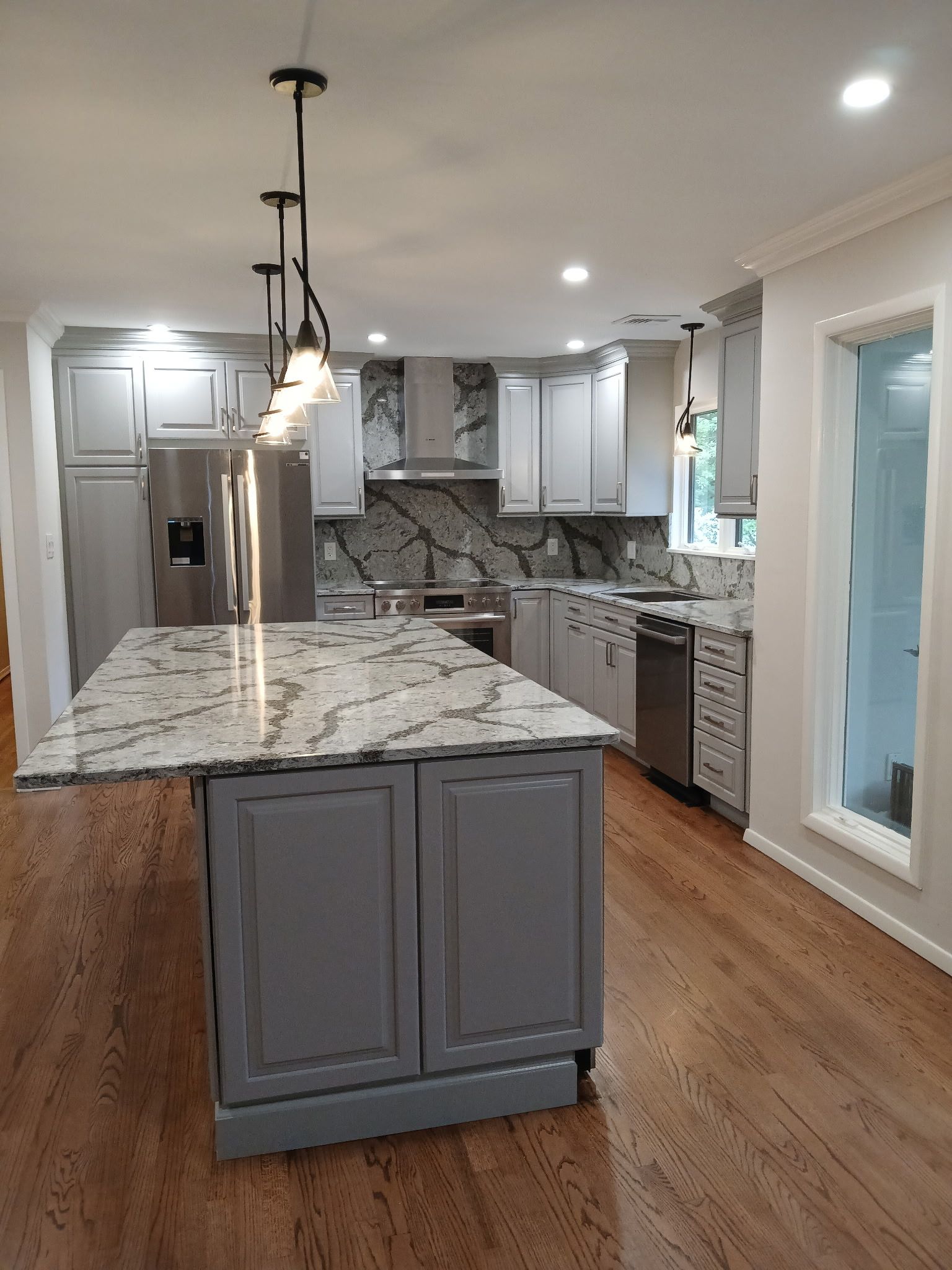 Modern kitchen with gray cabinets, marble countertops, stainless steel appliances, and wood floors.