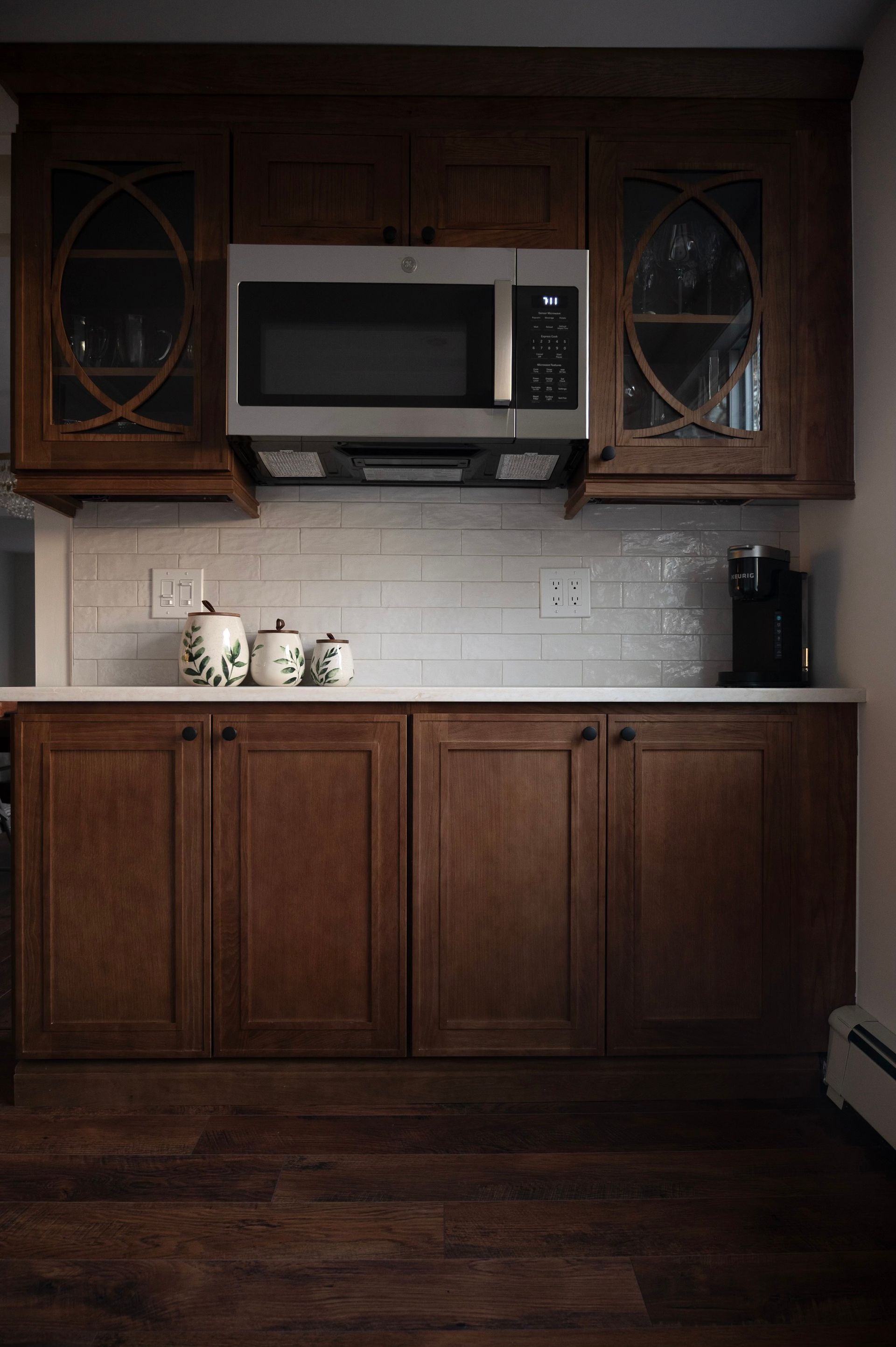 Kitchen cabinets: dark wood, microwave above, white backsplash, coffee maker, and ceramic jars.