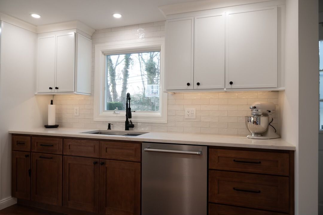 Kitchen with white upper cabinets and brown lower cabinets, stainless steel appliances, and a window above the sink.