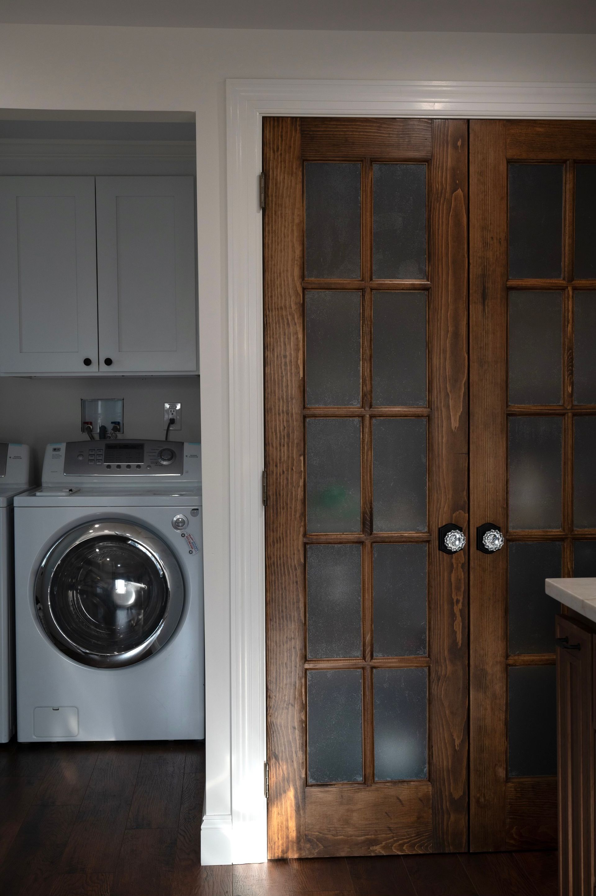 Brown, paneled doors with frosted glass lead to a laundry room with a white washing machine and cabinets.