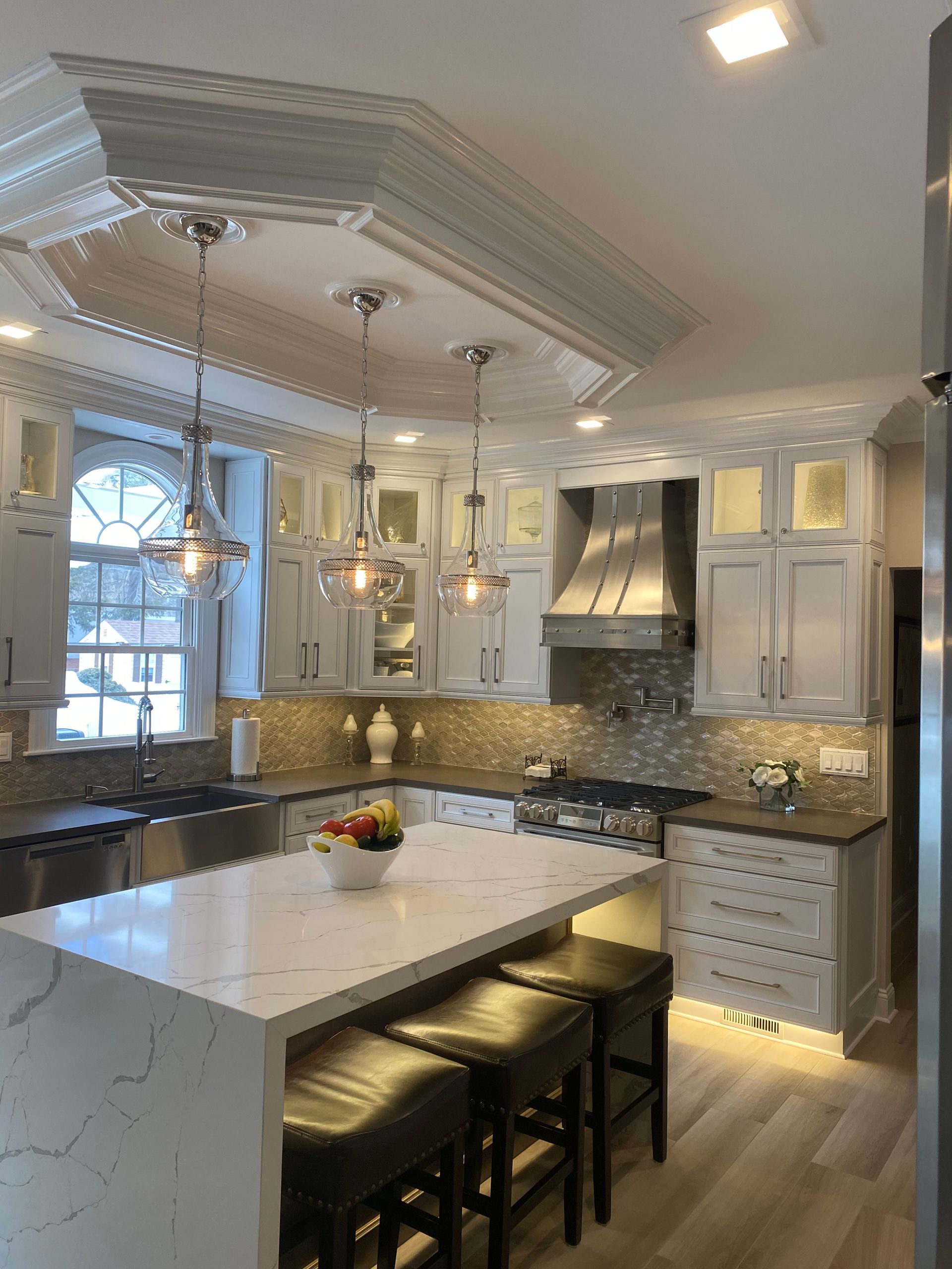 Elegant white kitchen with island, pendant lights, and stainless steel range hood.