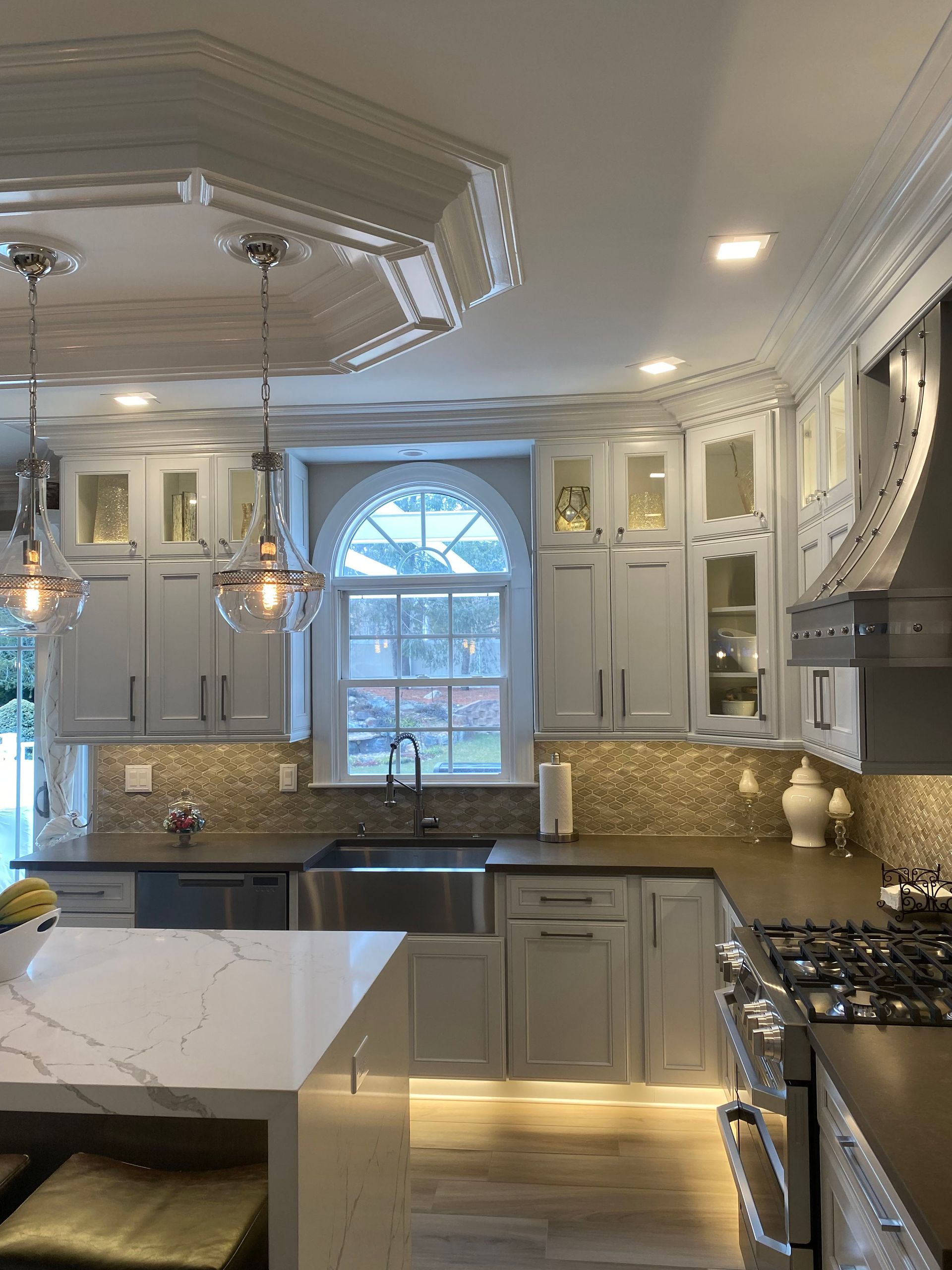 Elegant kitchen with light gray cabinets, white countertop island, and mosaic backsplash.