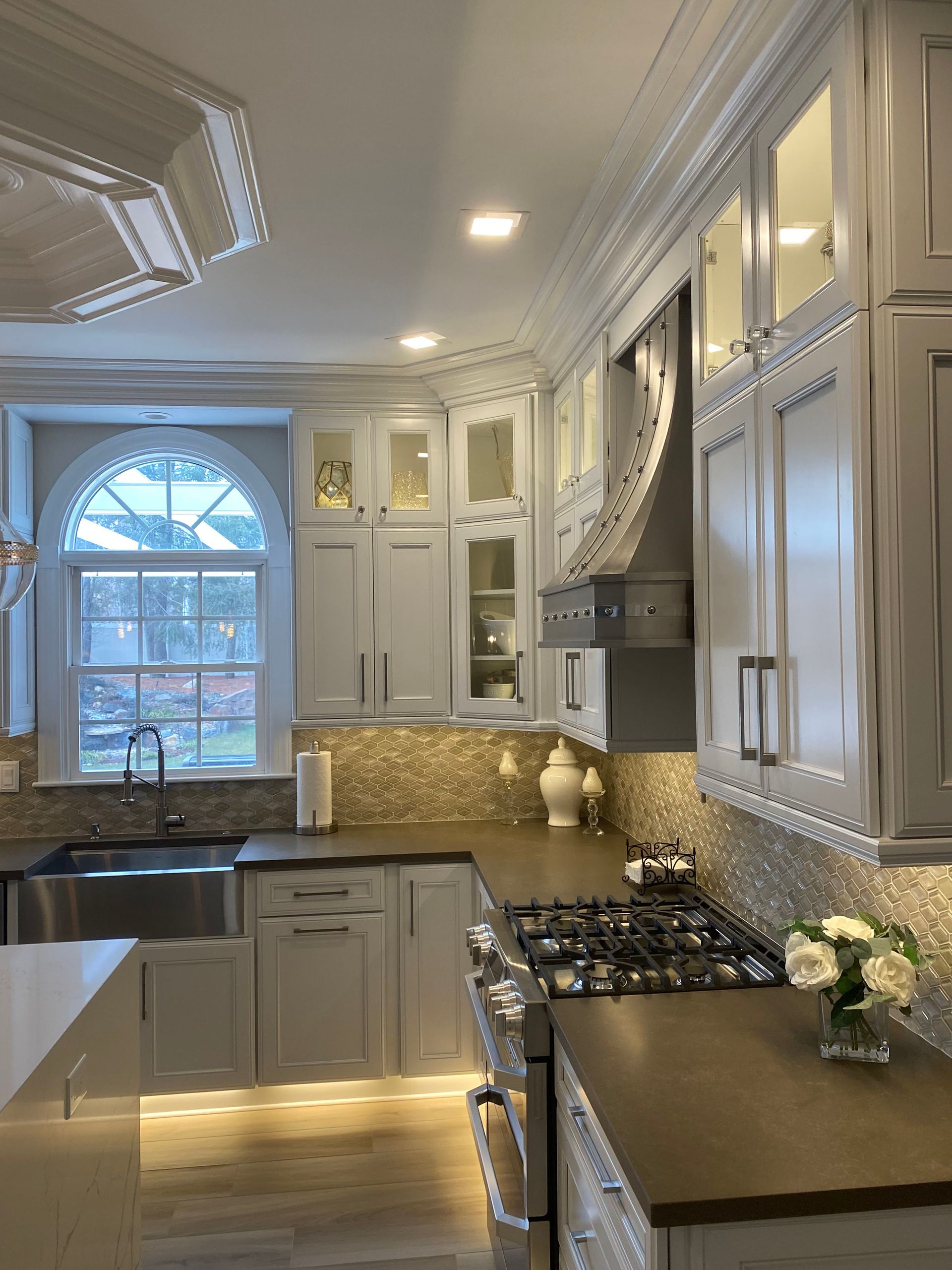 Elegant white kitchen with stainless steel appliances, mosaic tile backsplash, and arched window.