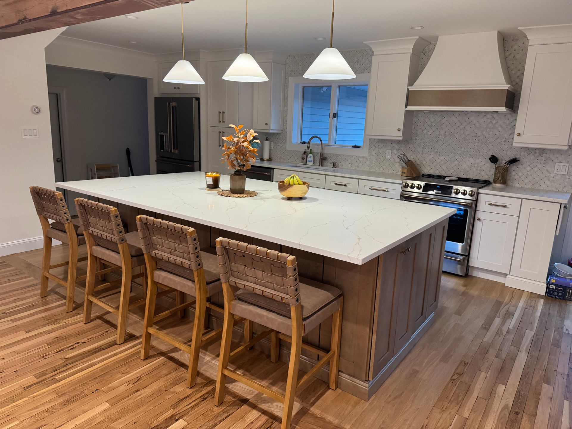 Kitchen with large island, seating, white countertops, stainless steel appliances, and wooden floors.