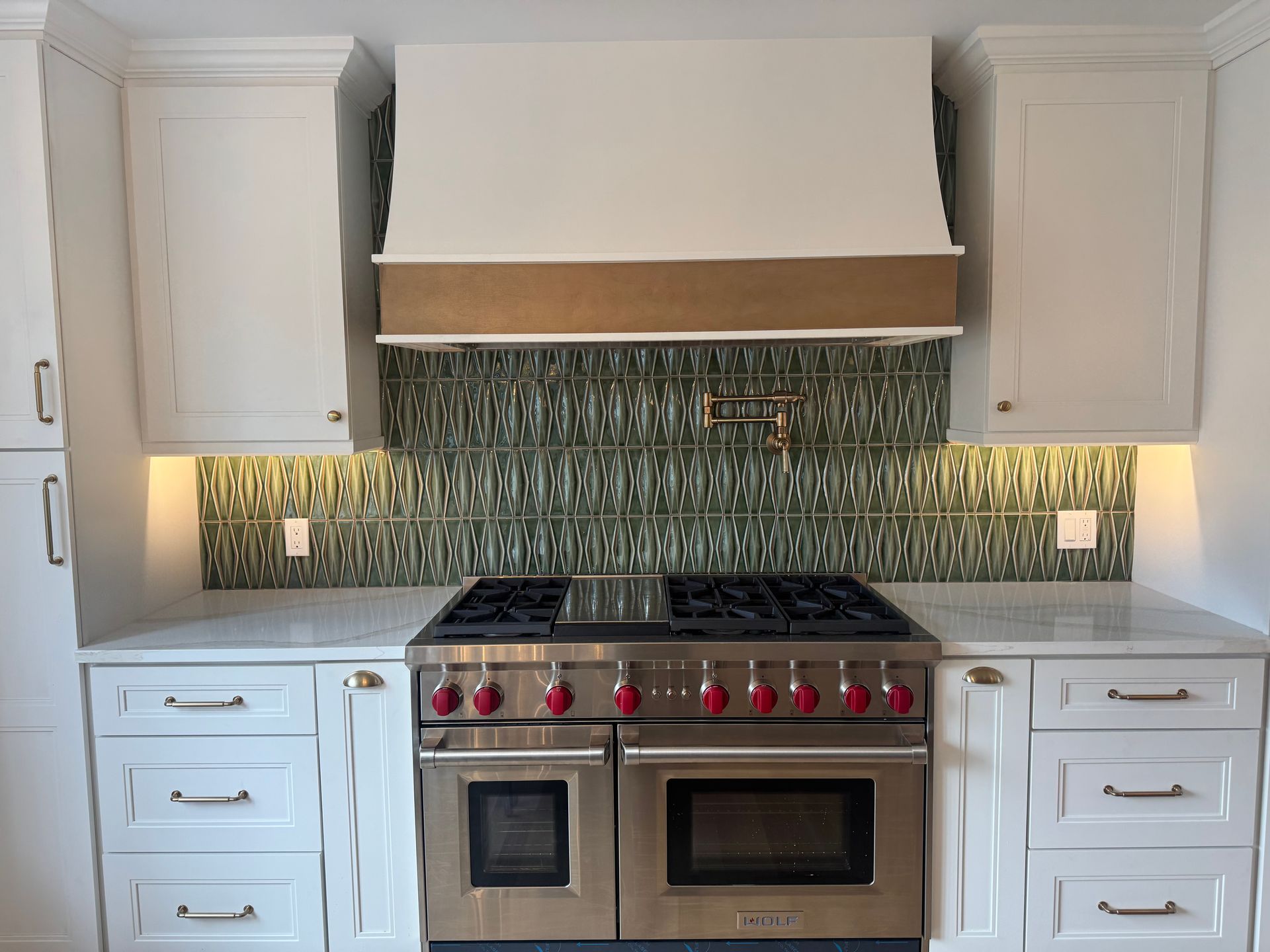 White kitchen with stainless steel oven, green tile backsplash, and white cabinets.