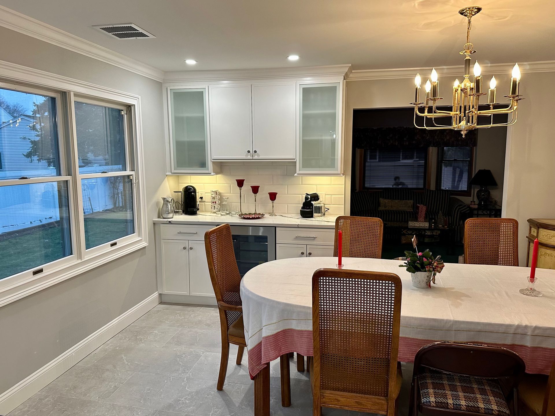A dining room with white cabinets, a round table set for a meal, and natural light from a window.