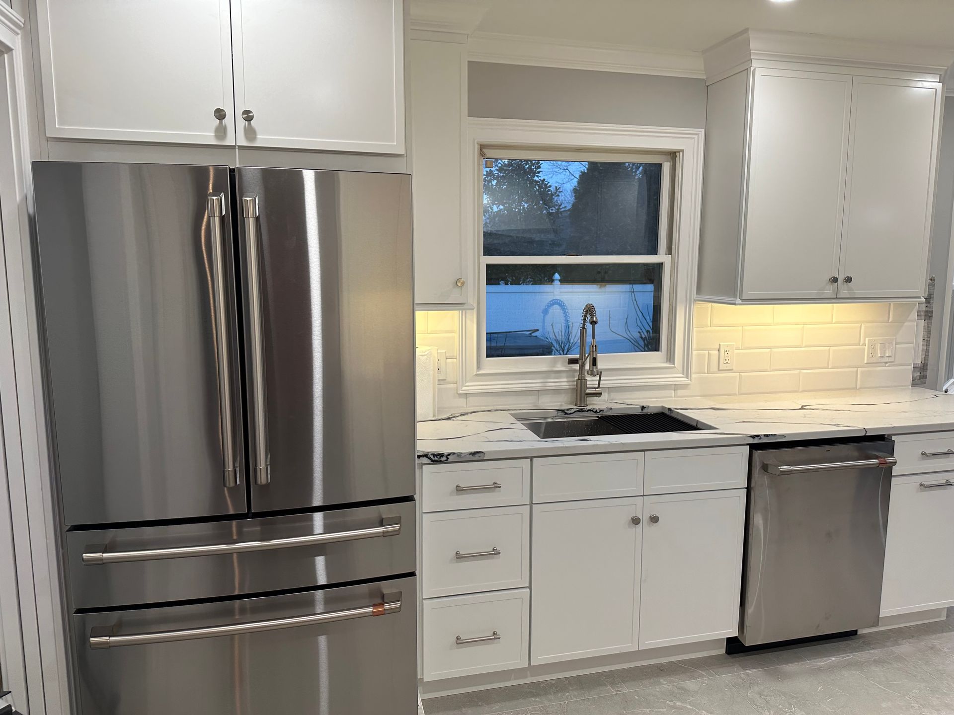 Modern kitchen with stainless steel appliances, white cabinets, and a window.
