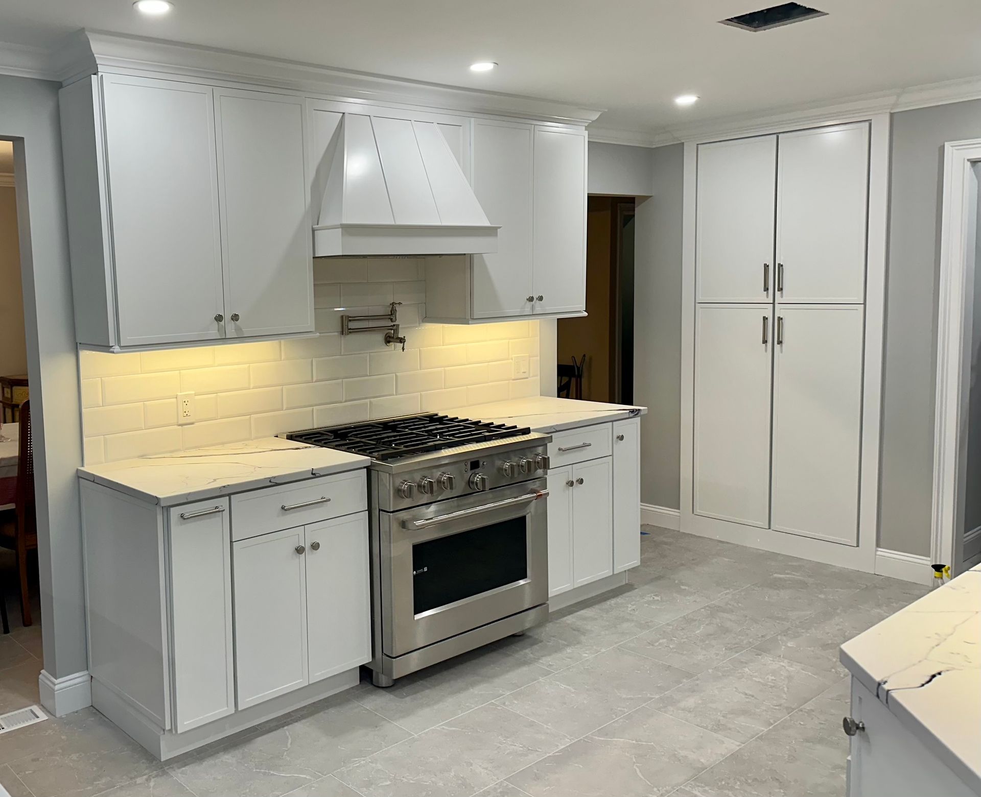 White kitchen with stainless steel appliances, white cabinets, and light gray flooring.