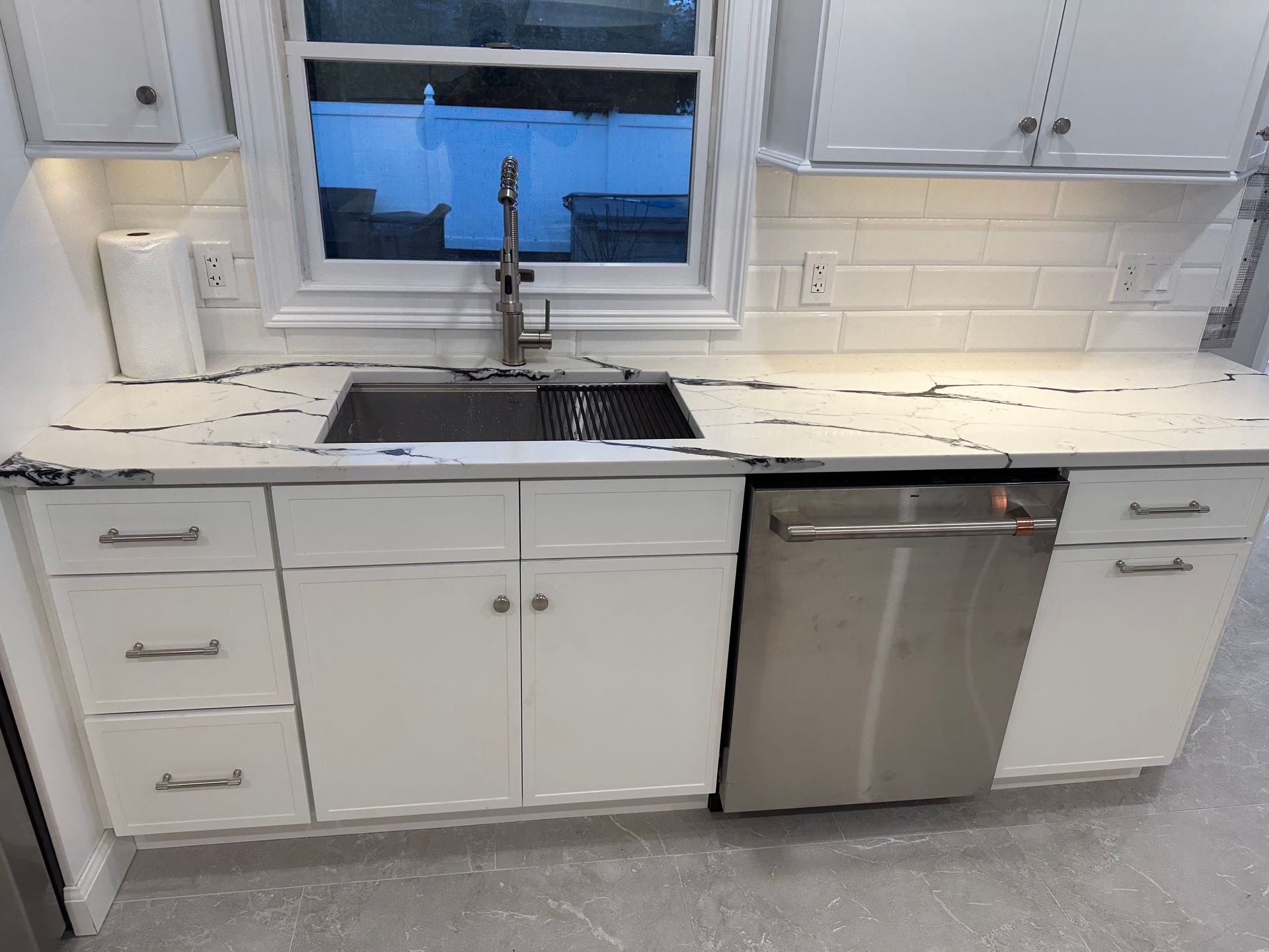 White kitchen with stainless steel sink and appliances; window over sink.