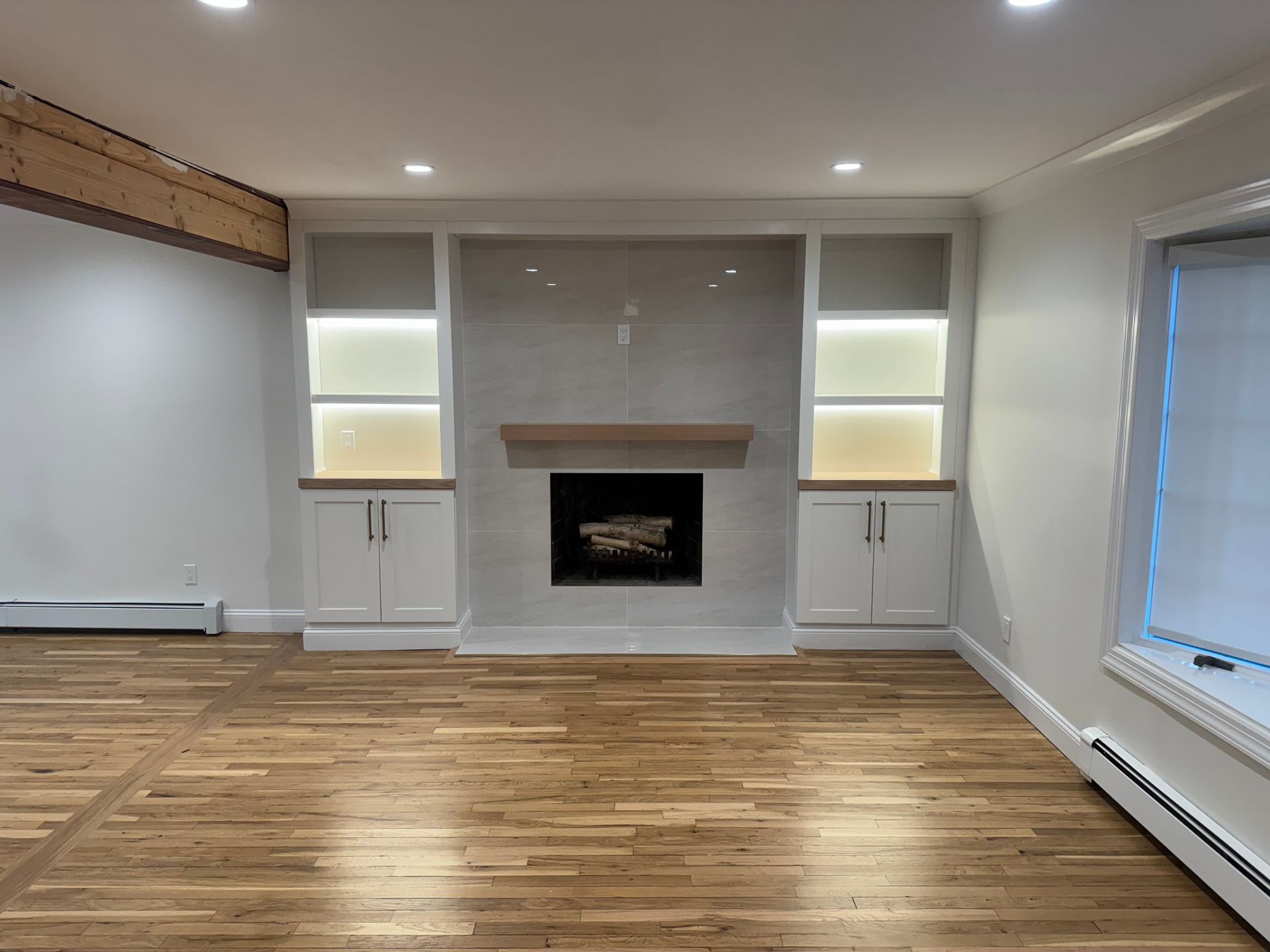 Living room with fireplace, white built-ins, and wood floors. Recessed lighting.