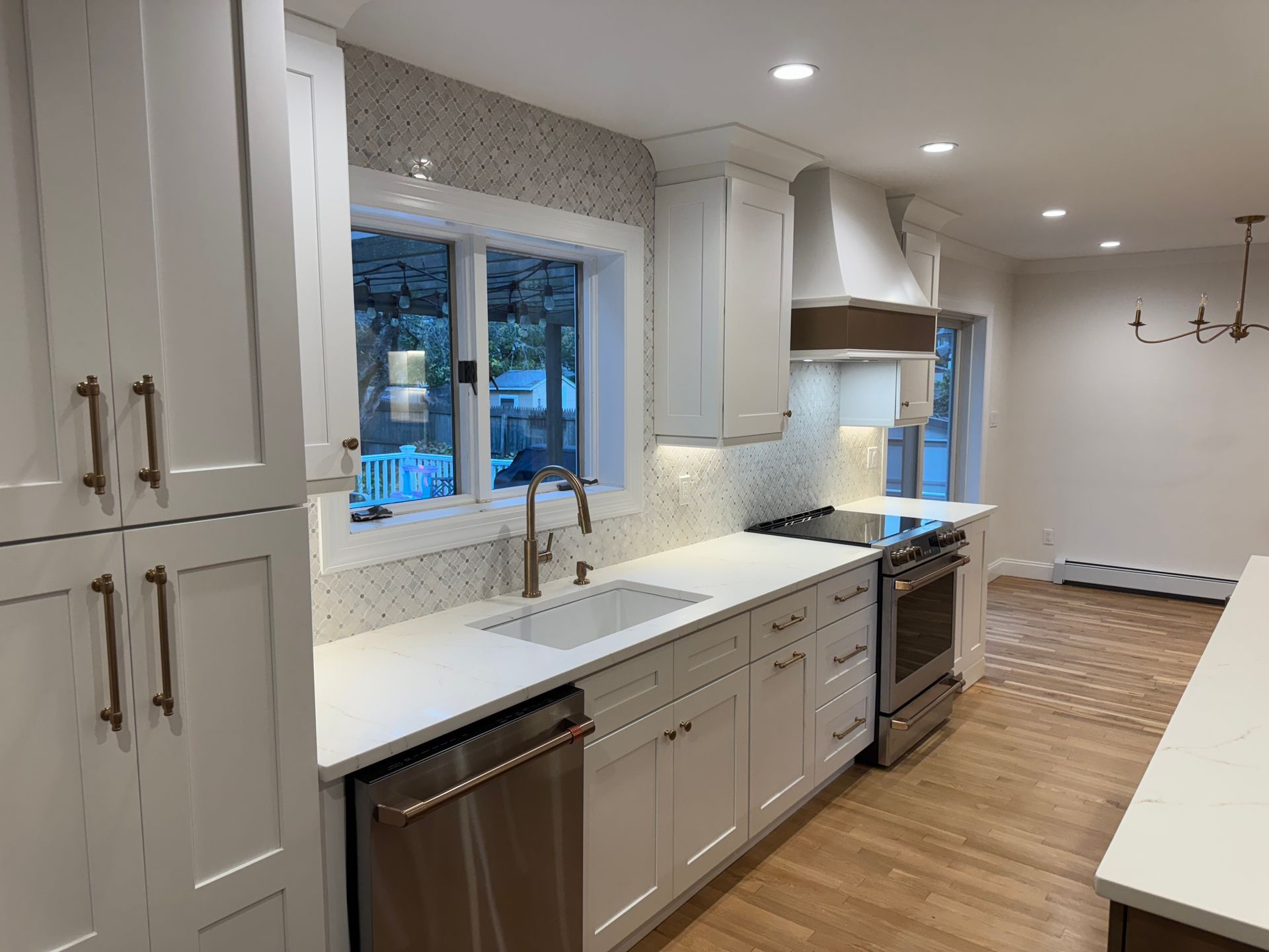 Modern white kitchen with stainless steel appliances, white countertops, and wood floors.