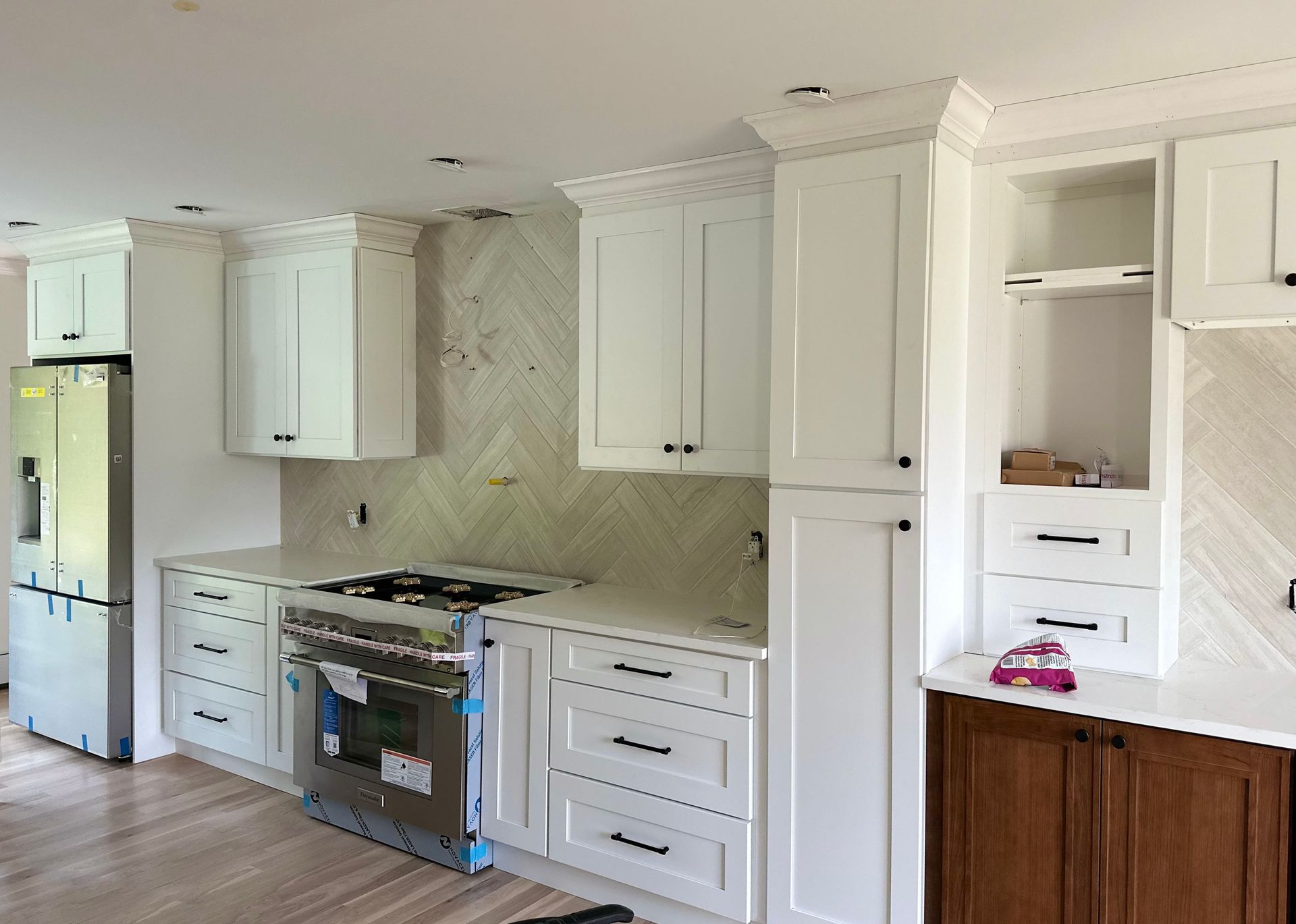 White kitchen cabinets, stainless steel range, and light countertops under construction.
