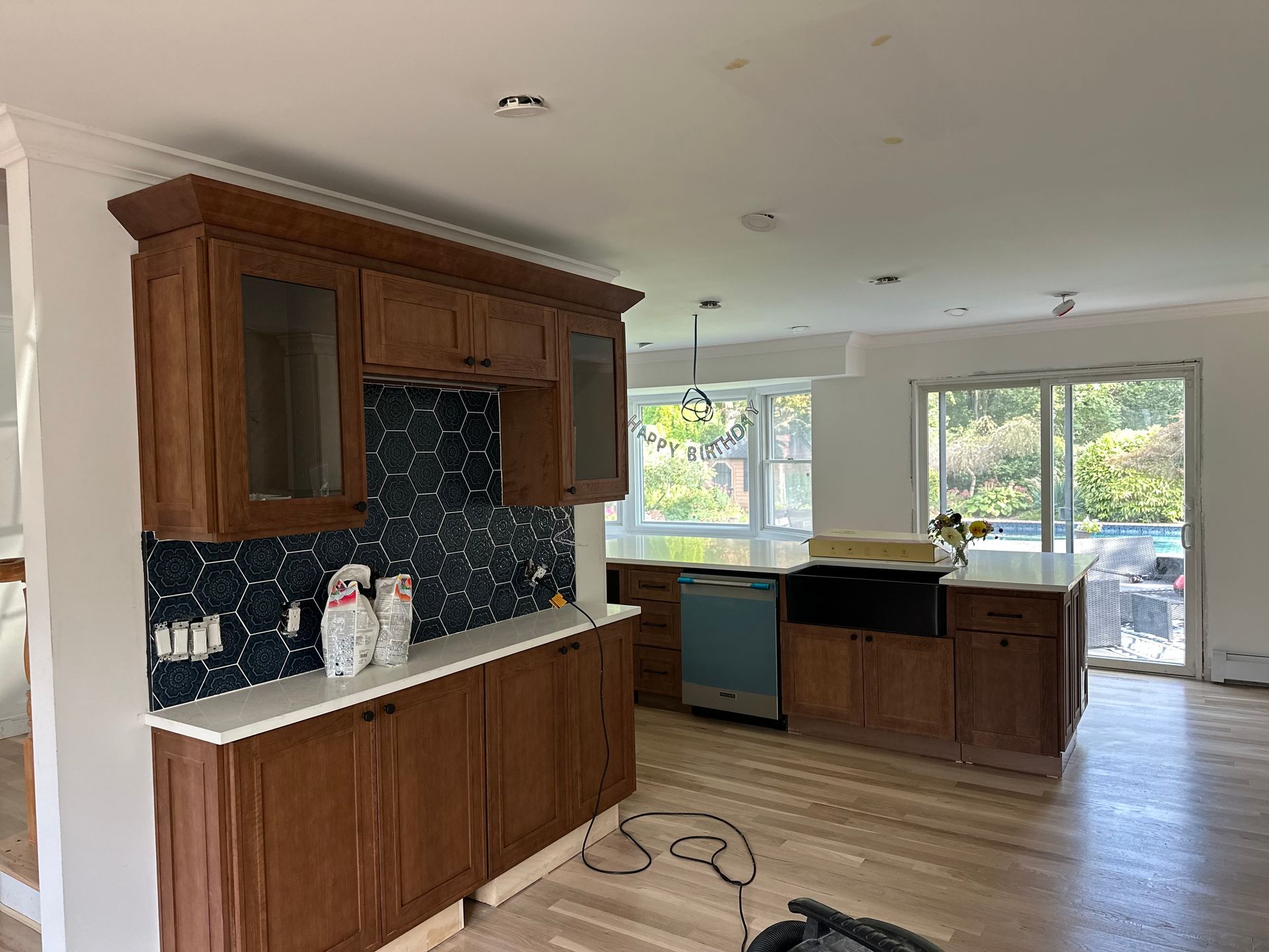 Kitchen renovation: brown cabinets, white countertops, blue tile backsplash, stainless steel dishwasher.